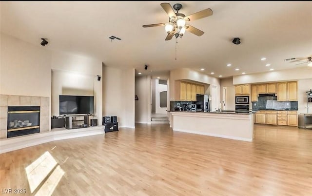 kitchen with stainless steel appliances, light wood-type flooring, backsplash, a tiled fireplace, and ceiling fan