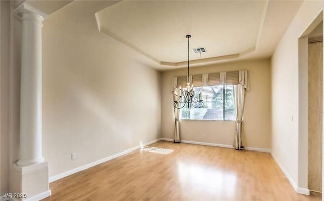 unfurnished dining area with hardwood / wood-style flooring, a raised ceiling, decorative columns, and a chandelier