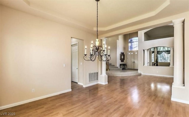 unfurnished dining area with wood-type flooring, a raised ceiling, and a notable chandelier