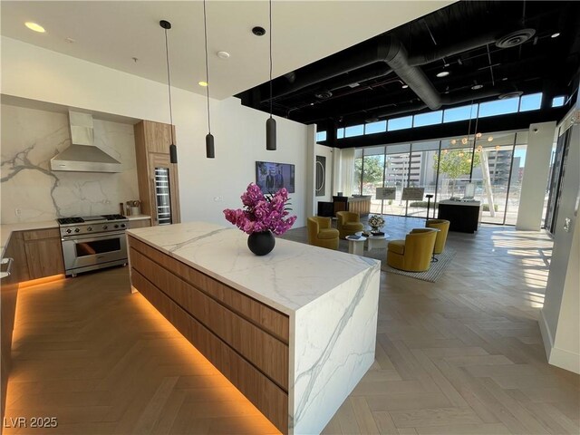 kitchen featuring a center island, parquet flooring, light stone counters, stainless steel range, and wall chimney range hood