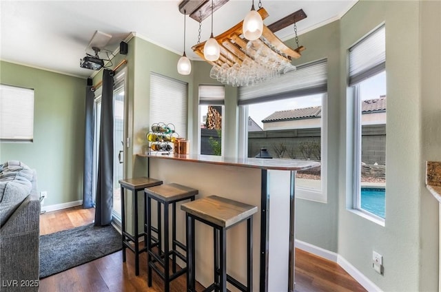 kitchen with decorative light fixtures, kitchen peninsula, a breakfast bar area, dark hardwood / wood-style flooring, and crown molding