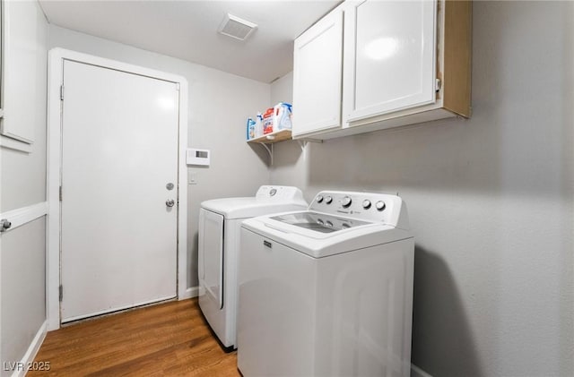 clothes washing area featuring separate washer and dryer, cabinets, and hardwood / wood-style floors