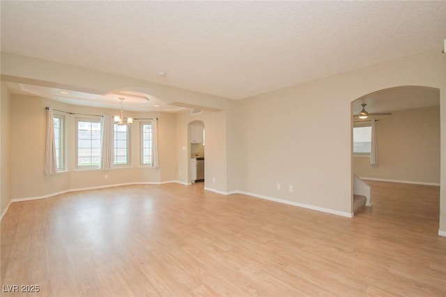 empty room with ceiling fan with notable chandelier, a textured ceiling, and light wood-type flooring