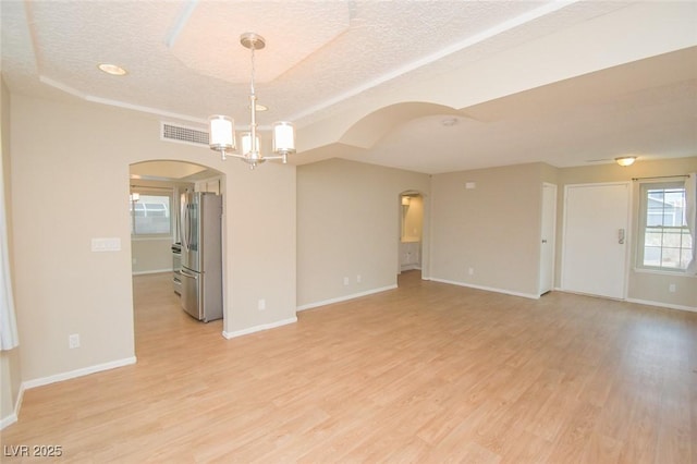 spare room with a textured ceiling, light hardwood / wood-style floors, a notable chandelier, and a tray ceiling