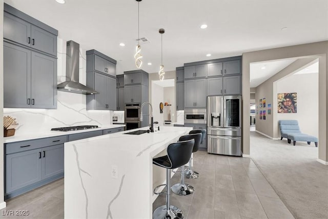 kitchen featuring a breakfast bar area, stainless steel appliances, light colored carpet, sink, and wall chimney range hood