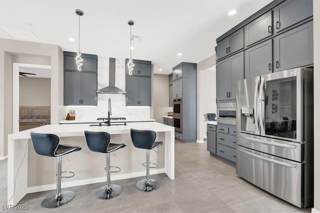 kitchen with a kitchen island with sink, stainless steel appliances, pendant lighting, wall chimney range hood, and backsplash