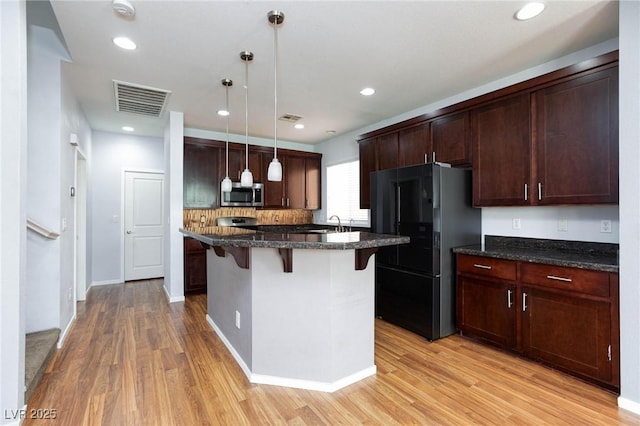 kitchen featuring pendant lighting, a breakfast bar area, a kitchen island with sink, light hardwood / wood-style floors, and black fridge