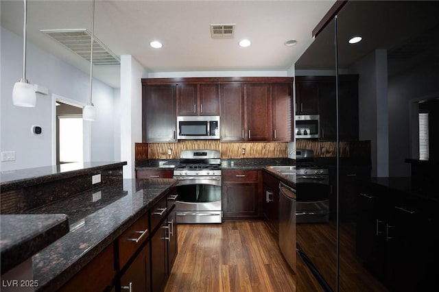 kitchen featuring sink, dark stone countertops, dark hardwood / wood-style flooring, hanging light fixtures, and stainless steel appliances