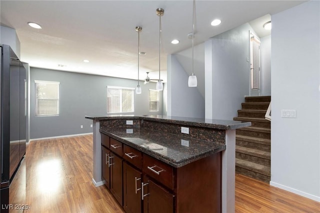 kitchen featuring pendant lighting, light hardwood / wood-style flooring, dark stone countertops, fridge, and a kitchen island