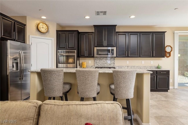 kitchen with stainless steel appliances, a kitchen bar, and light stone countertops