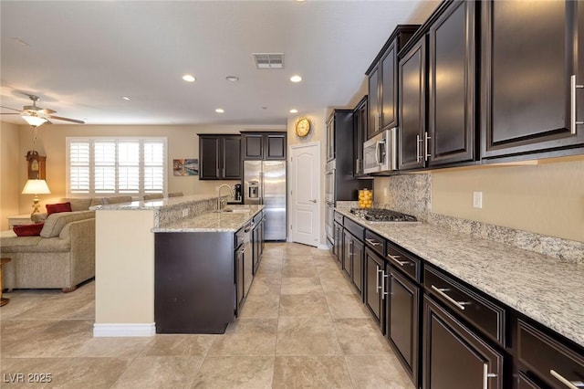 kitchen featuring sink, light stone counters, ceiling fan, dark brown cabinetry, and appliances with stainless steel finishes