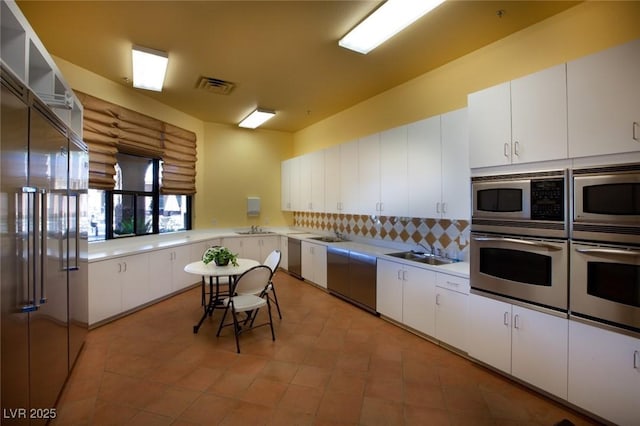 kitchen with appliances with stainless steel finishes, rustic walls, decorative backsplash, white cabinets, and sink