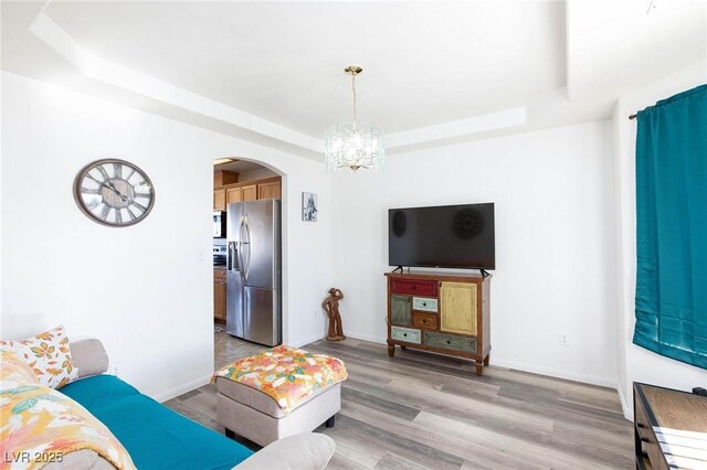 living room featuring light hardwood / wood-style floors, a raised ceiling, and a notable chandelier