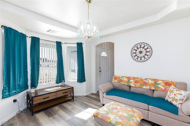 living room with wood-type flooring, a tray ceiling, and a notable chandelier