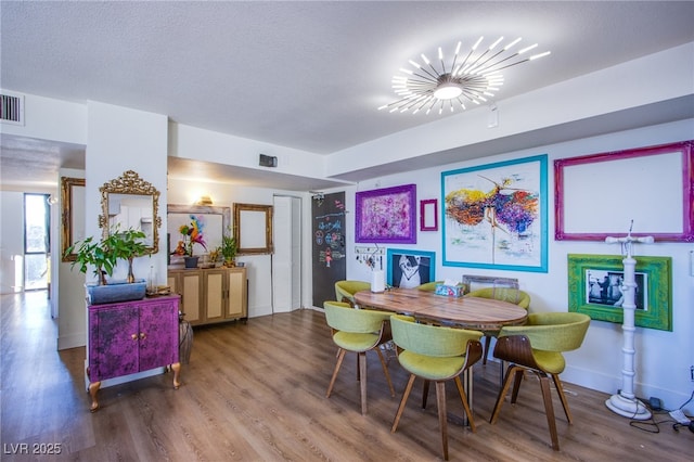 dining area with a textured ceiling, wood-type flooring, and an inviting chandelier