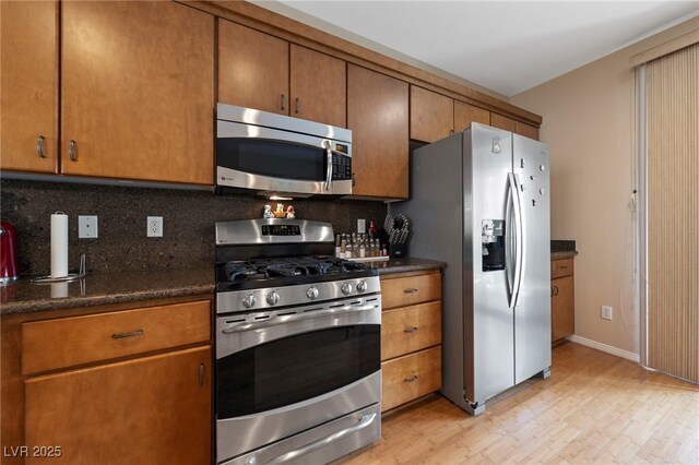 kitchen featuring appliances with stainless steel finishes, light wood-type flooring, dark stone counters, and backsplash