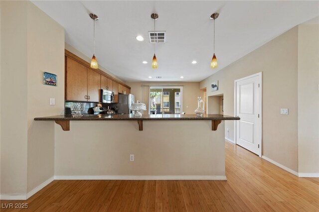 kitchen with stainless steel appliances, light wood-type flooring, hanging light fixtures, and kitchen peninsula