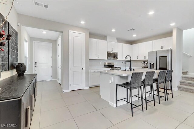 kitchen with stainless steel appliances, an island with sink, a kitchen bar, sink, and white cabinetry