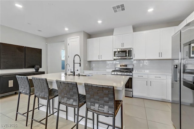 kitchen with a center island with sink, stainless steel appliances, sink, white cabinetry, and backsplash