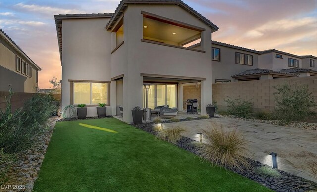 back house at dusk with a patio and a lawn