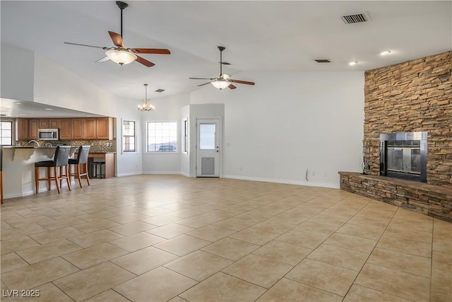 unfurnished living room with lofted ceiling, ceiling fan with notable chandelier, a fireplace, and light tile patterned floors