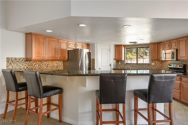 kitchen with stainless steel appliances, dark stone counters, light tile patterned floors, and a kitchen bar