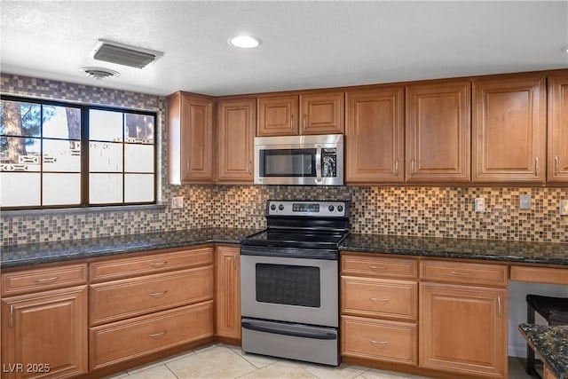 kitchen with stainless steel appliances, dark stone counters, light tile patterned floors, and tasteful backsplash