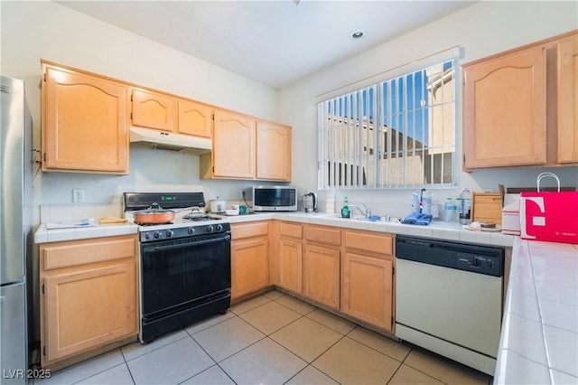 kitchen with stainless steel appliances, sink, light brown cabinets, light tile patterned floors, and tile counters