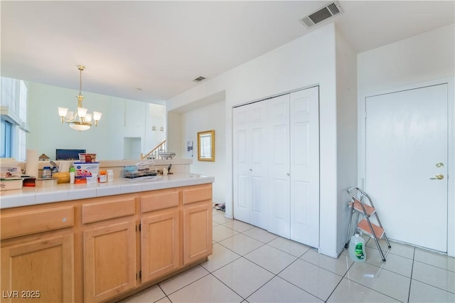 kitchen with light brown cabinets, light tile patterned floors, tile counters, a chandelier, and pendant lighting