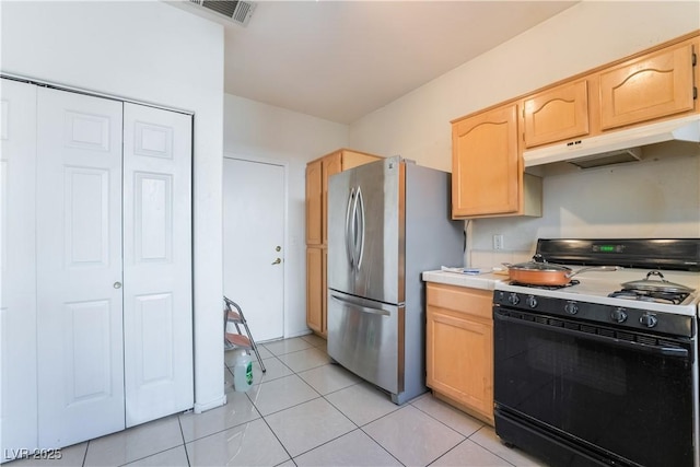 kitchen featuring light tile patterned floors, gas range oven, light brown cabinets, and stainless steel refrigerator