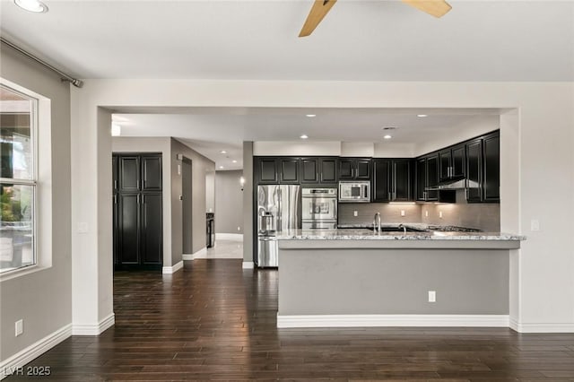 kitchen featuring appliances with stainless steel finishes, kitchen peninsula, light stone countertops, dark wood-type flooring, and decorative backsplash