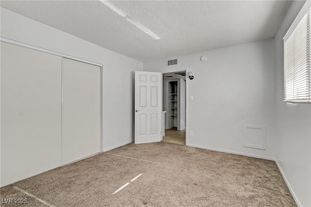 unfurnished bedroom featuring a textured ceiling, a closet, and light carpet