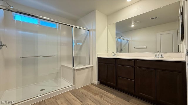 bathroom featuring double vanity, a stall shower, wood finished floors, and visible vents