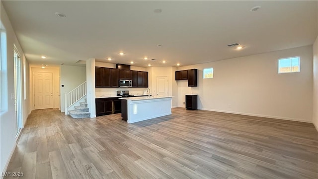 kitchen featuring stainless steel appliances, visible vents, light wood-style floors, open floor plan, and dark brown cabinets