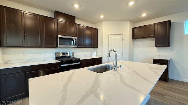 kitchen featuring light stone counters, stainless steel appliances, a sink, dark brown cabinets, and wood finished floors