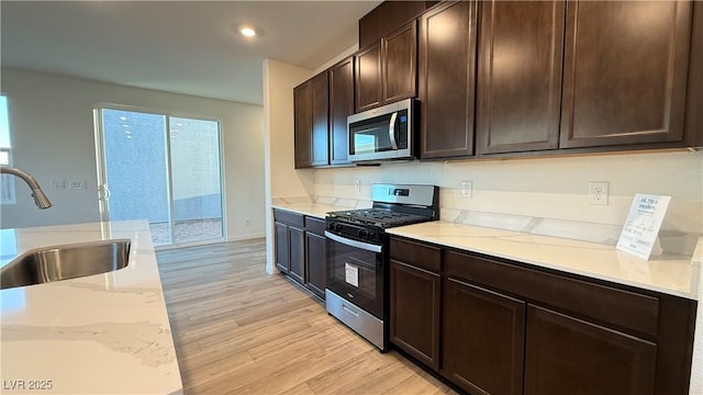 kitchen featuring appliances with stainless steel finishes, light wood-style floors, a sink, dark brown cabinets, and light stone countertops