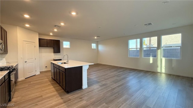 kitchen featuring light wood-type flooring, visible vents, a sink, and black gas range oven