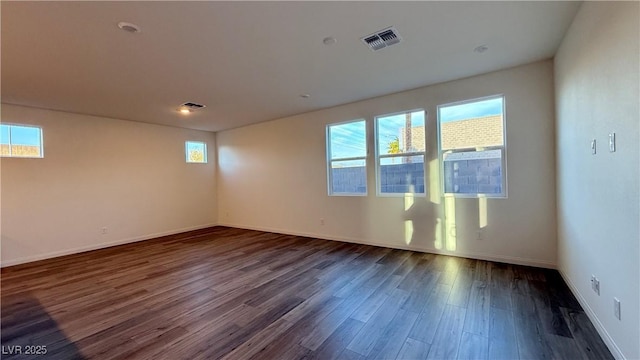 unfurnished room featuring dark wood-type flooring, visible vents, and baseboards