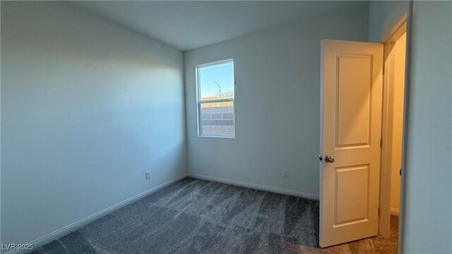 spare room with dark carpet and baseboards