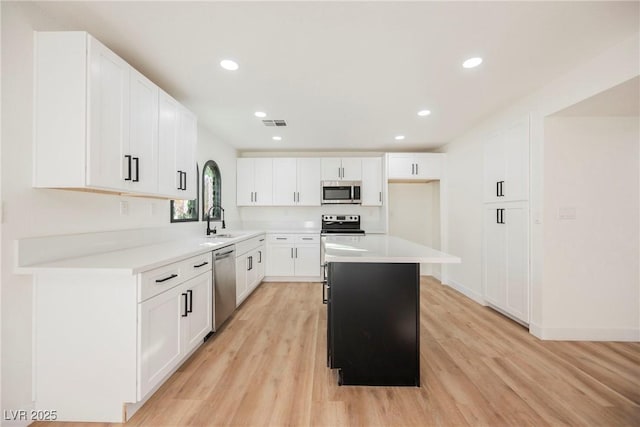 kitchen featuring stainless steel appliances, a kitchen island, white cabinets, light hardwood / wood-style flooring, and sink