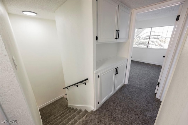 hall with a textured ceiling and dark colored carpet