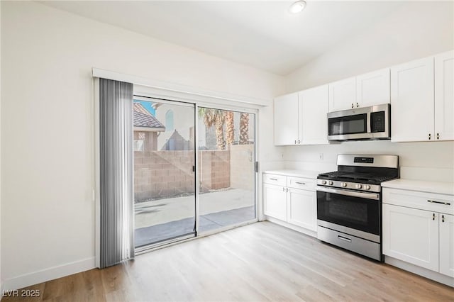 kitchen with stainless steel appliances, white cabinetry, vaulted ceiling, and light wood-type flooring