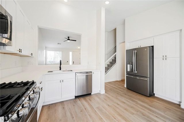 kitchen with white cabinets, stainless steel appliances, light wood-type flooring, ceiling fan, and sink