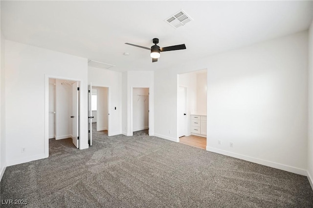 unfurnished bedroom with ceiling fan, a walk in closet, ensuite bath, and carpet flooring