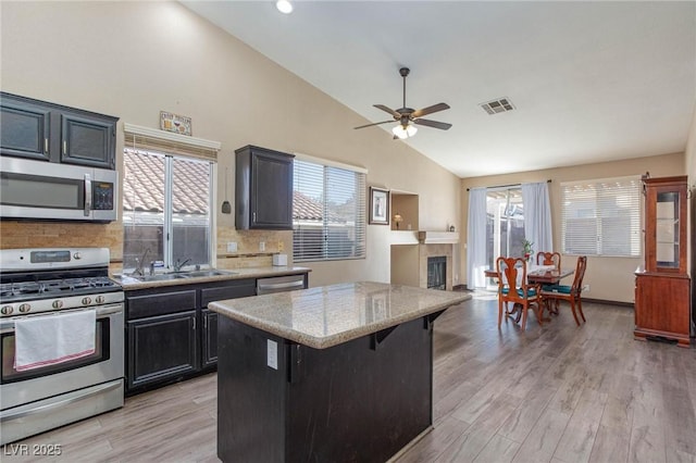 kitchen with a center island, decorative backsplash, light wood-type flooring, appliances with stainless steel finishes, and a kitchen breakfast bar