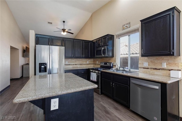 kitchen with dark wood-type flooring, a center island, stainless steel appliances, decorative backsplash, and sink