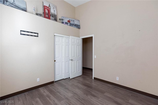 unfurnished bedroom with a high ceiling, a closet, and wood-type flooring