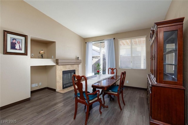 dining room featuring a tile fireplace, dark wood-type flooring, and vaulted ceiling