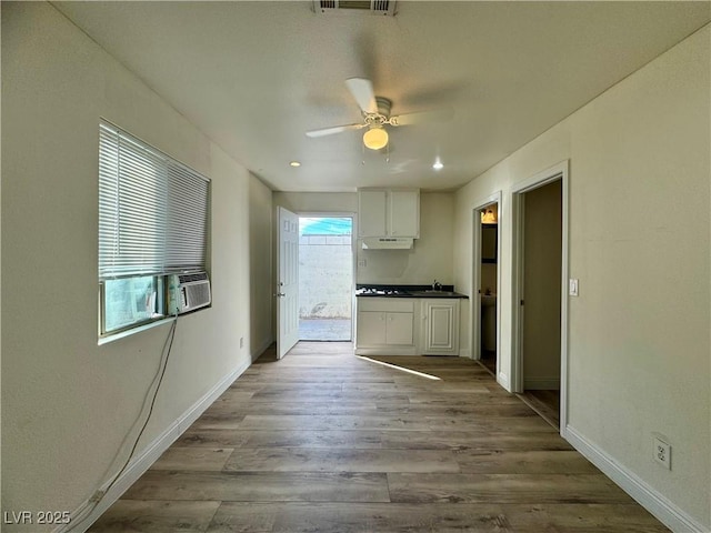 kitchen featuring light wood-type flooring, cooling unit, white cabinetry, ceiling fan, and sink