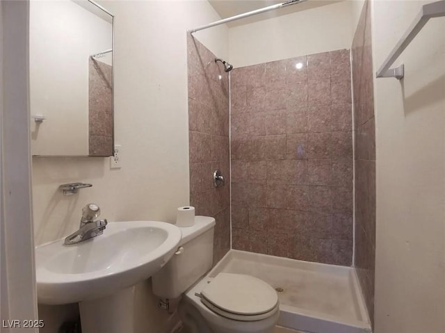 bathroom featuring sink, a tile shower, and toilet